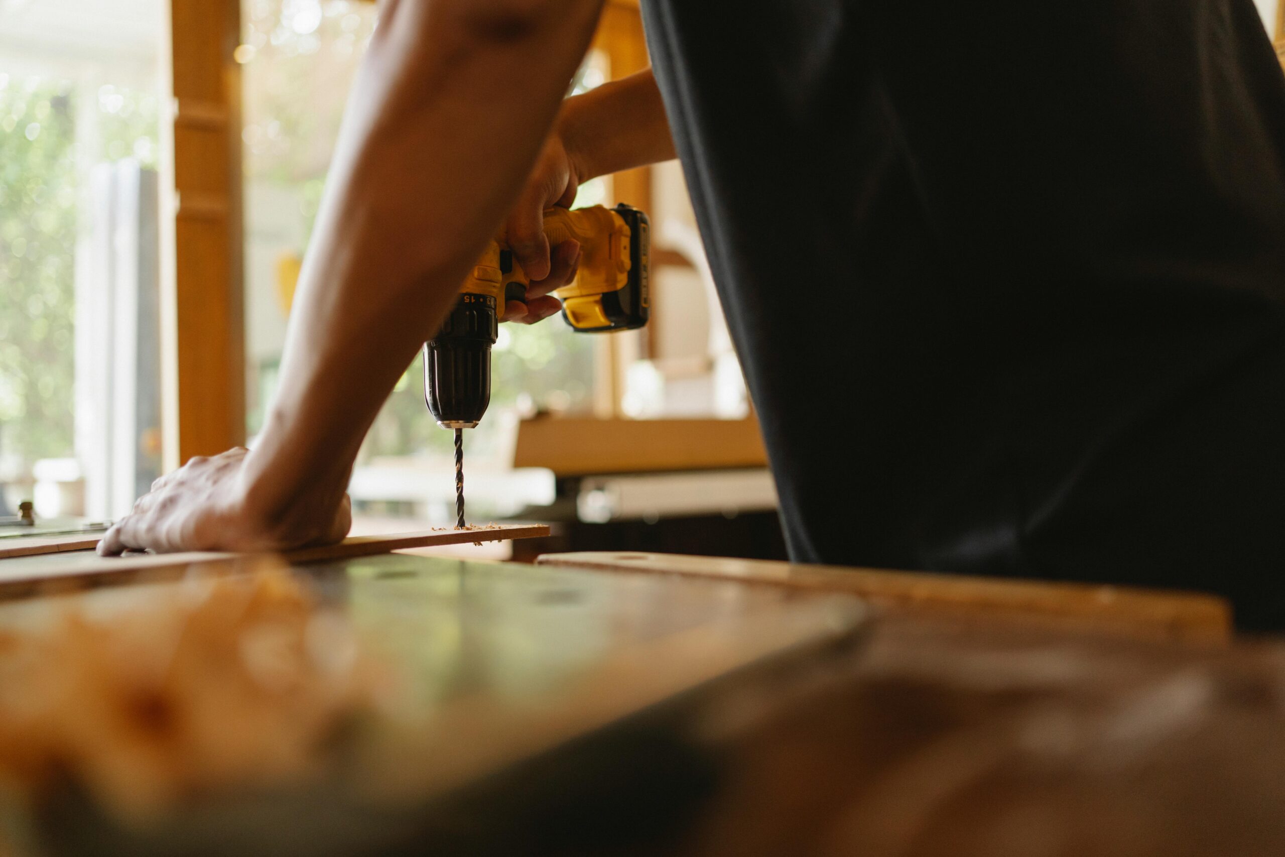 A skilled carpenter uses an electric drill on a wooden plank indoors, highlighting craftsmanship.